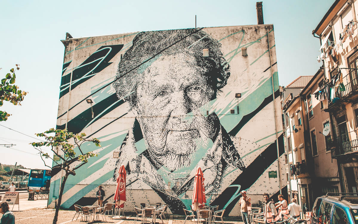 street art on wall of old woman next to a cafe in porto portugal